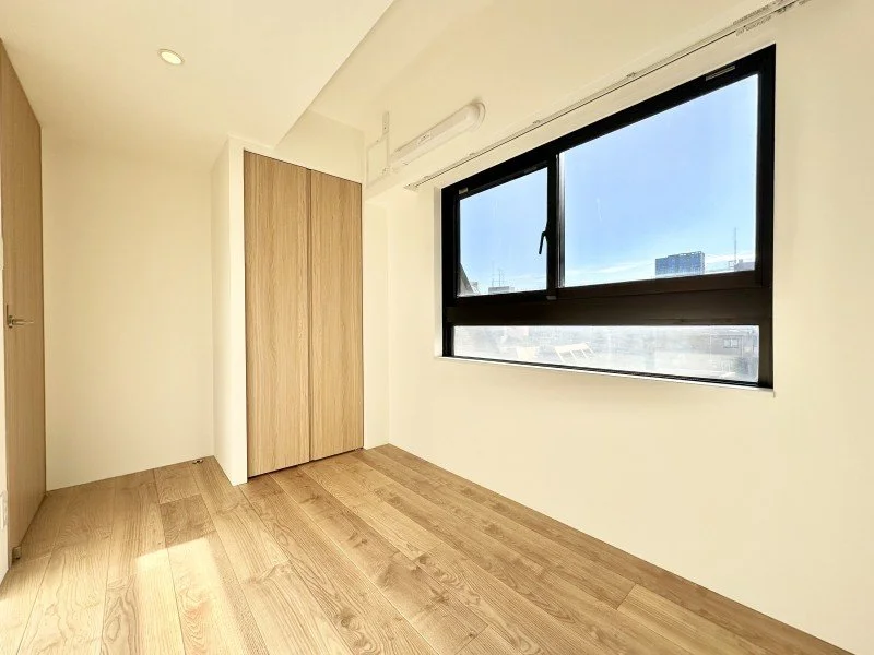 明るい窓のある空き部屋、木製の床とクローゼット、外の青空が見える