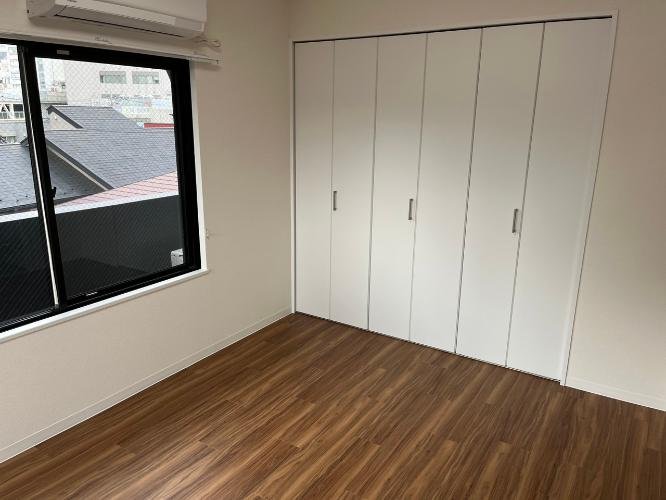 空の部屋に白いクローゼットと窓があり、木製のフロアが敷かれている
