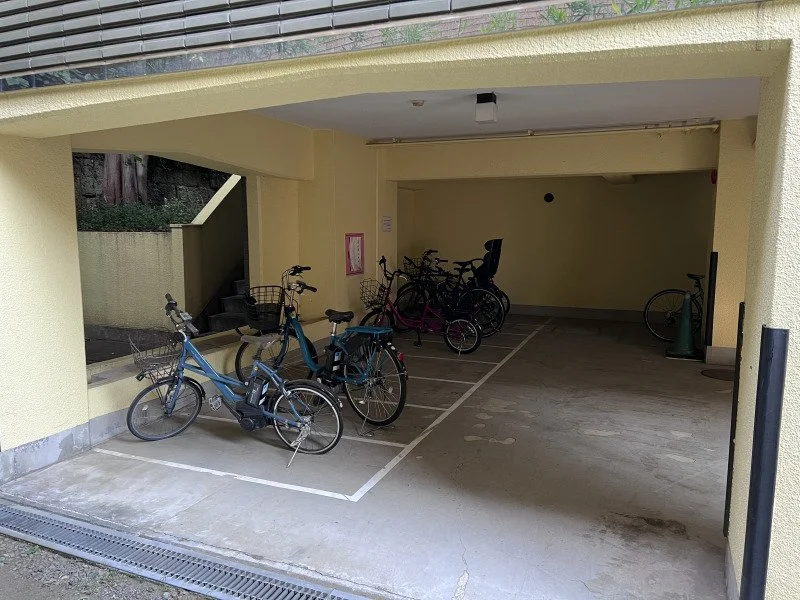 黄色い建物の駐輪場に自転車が置かれている。複数の自転車とバイクが収納されている。