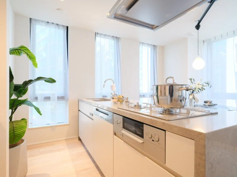 明るいキッチンで、窓から自然光が差し込み、シンクとガスコンロ、調理用の大きな鍋が置かれている。