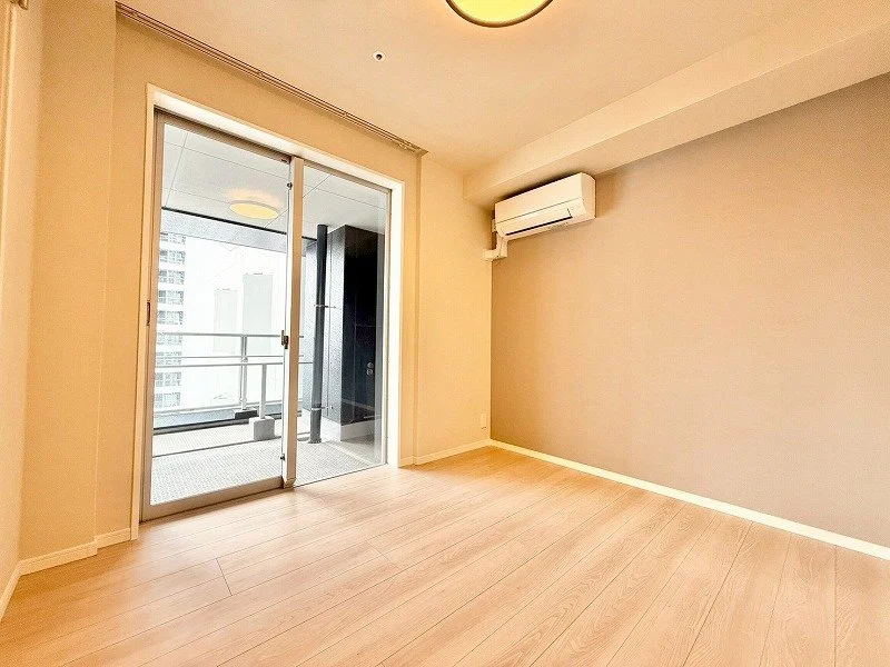 広々とした空室で、バルコニーに面したガラスドアと壁掛けエアコンがある明るい部屋