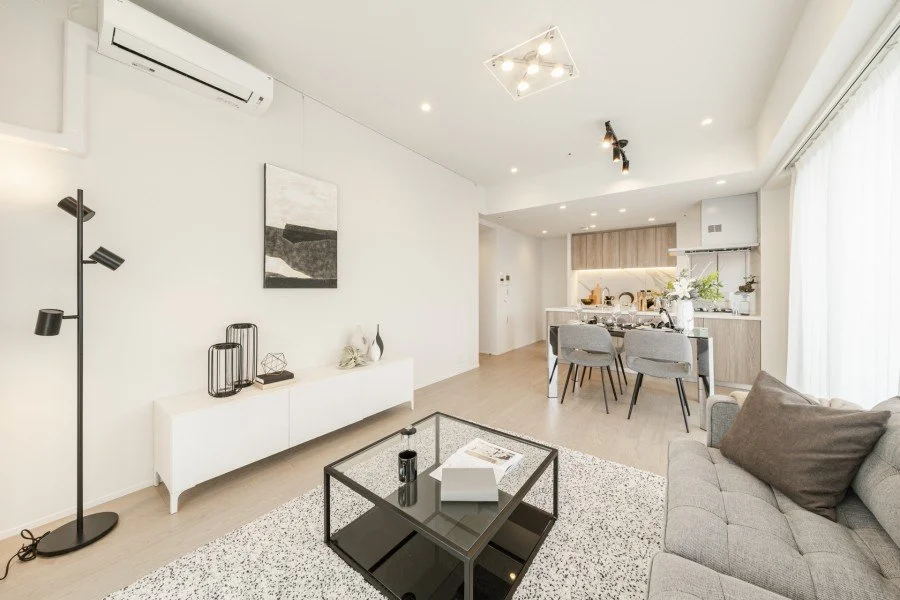 白と木材を基調としたリビングとキッチンのモダンな居住空間、ソファ、ローテーブル、ダイニングセット、窓のカーテンあり