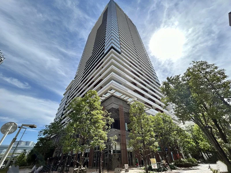 高層ビルと青空と緑の木々。低層部分に人々と街路樹が見える都市風景。