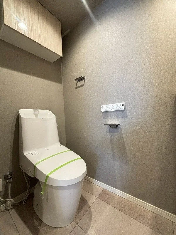 新しい洋式トイレと壁に取り付けられた紙巻き器とコントロールパネルのあるウォッシュレット付きのトイレルームの interior.