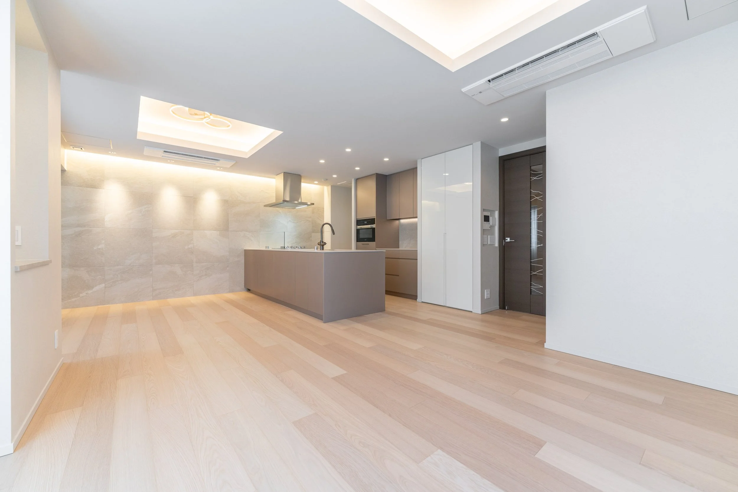 明るい開放的なリビングルームとキッチンの空間が見えるモダンなインテリア。木製の床、白い壁天井、調和のとれた家具と照明に囲まれている。