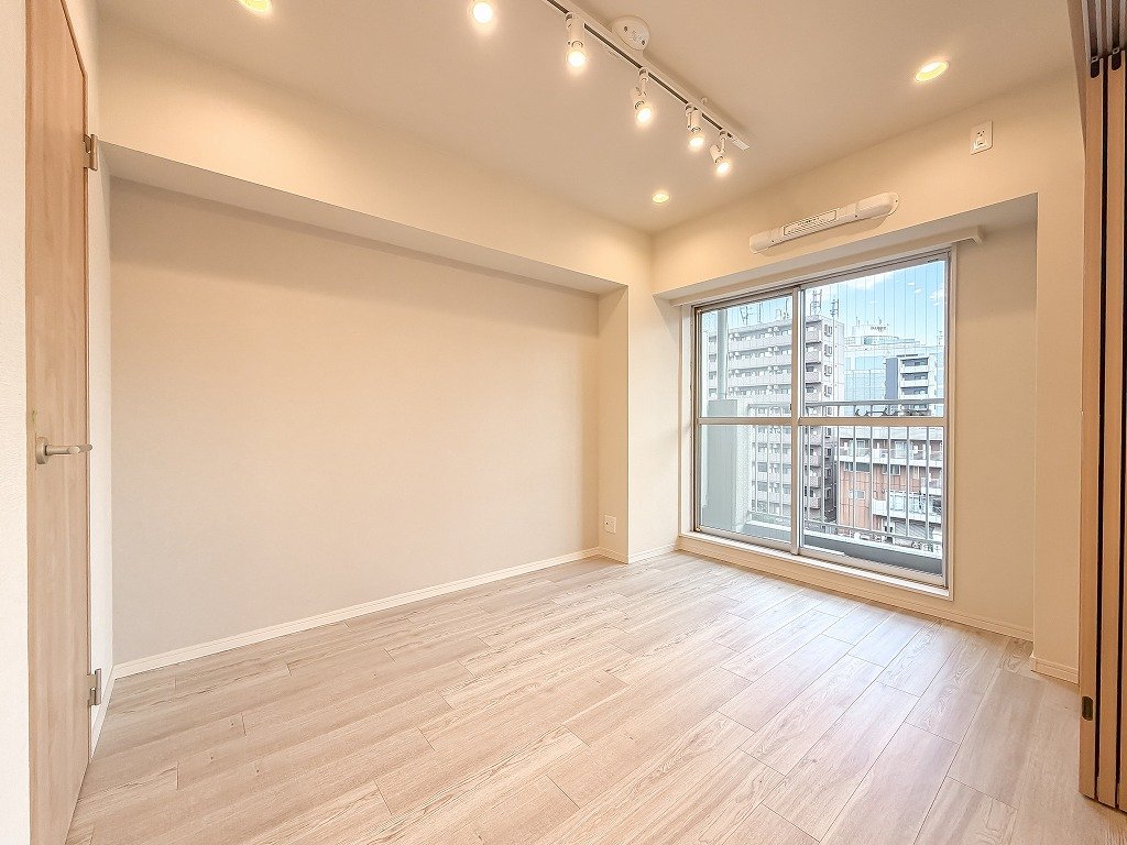 明るい部屋、木の床、白い壁、大きな窓から都市の景色が見える、天井に照明とエアコンが設置されている
