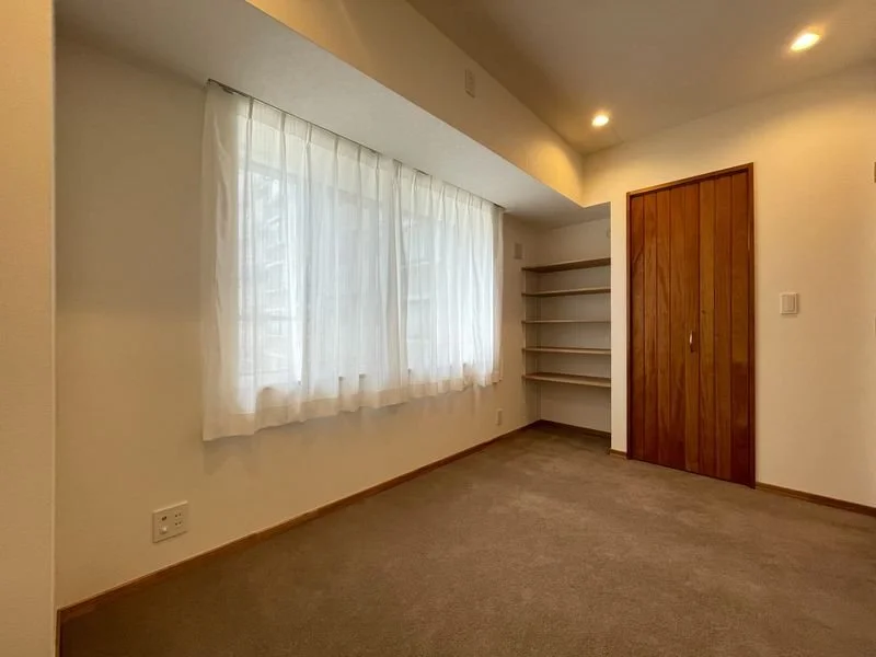 日光が差し込む窓辺の空き部屋、白いカーテンと木製の棚とドアがある部屋の写真
