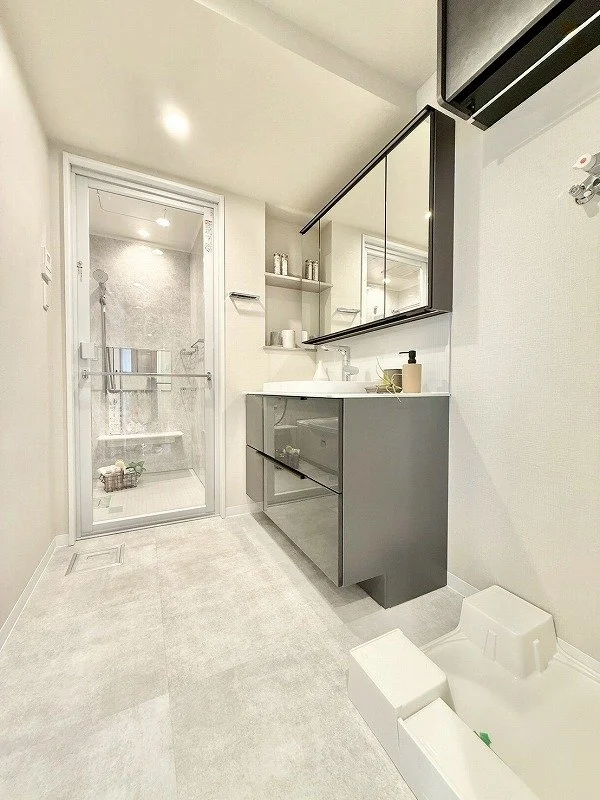 白とグレーのモダンな浴室と洗面台、鏡と棚が配置された空間。右側に洗濯機置き場のスペースもある。