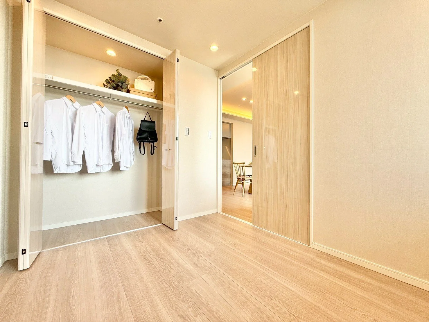 木製の引き戸が開いたクローゼットの中に、白いシャツとバッグが掛かっている。