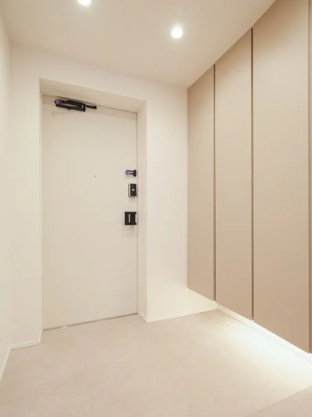 白いドアと折りたたみ式の壁面収納があるシンプルなエントランスホール