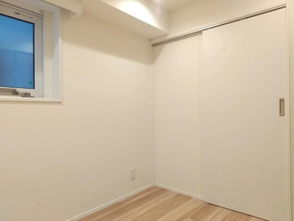 白い壁と木製フローリング、引き戸のクローゼット、窓のある空き部屋