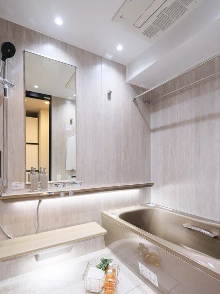 浴室の洗面台と鏡、バスタブ、天井の照明と換気扇がある室内の写真