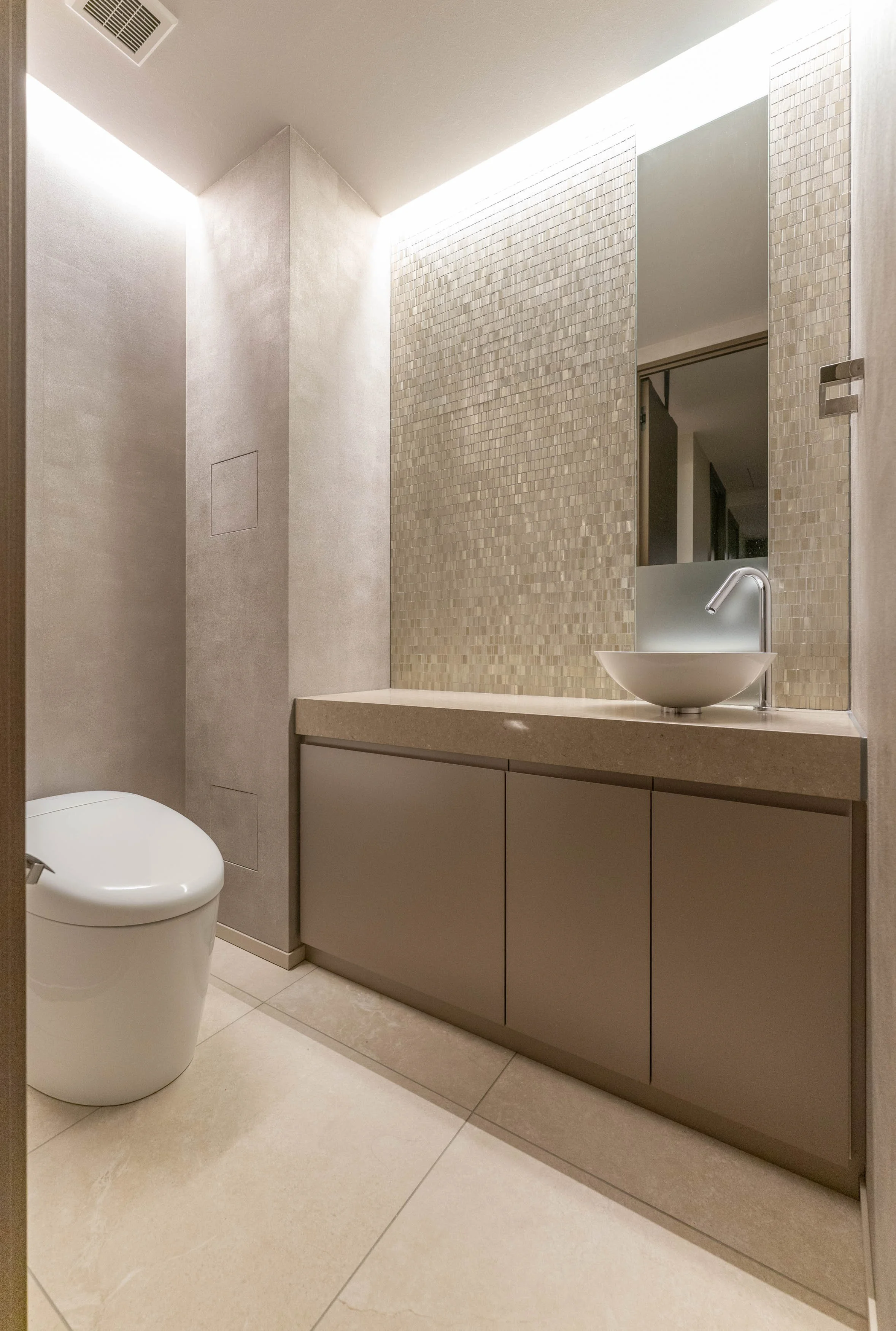 シンプルで現代的なデザインのトイレの内装。便器と洗面台、鏡と収納棚が設置されている。