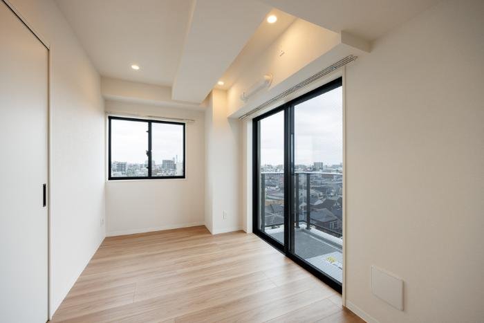 明るい空間の部屋、木製フローリングと大きな窓、バルコニーへのガラスドアがある。