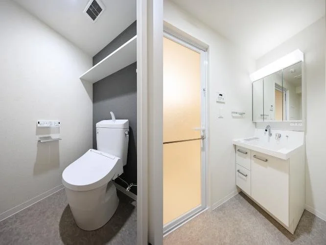 トイレと洗面台のあるバスルームの内装。トイレは左側にあり、右側には洗面台と鏡が設置されている。