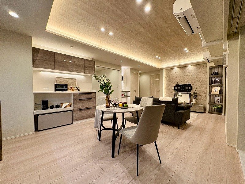 モダンなリビングルームとキッチンのオープンプラン居住空間、ダイニングテーブルと椅子、ソファ、棚に装飾品と植物が配置されている