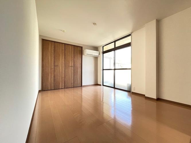 空の部屋で、大きな窓と木製のクローゼット、エアコンが備わっている。