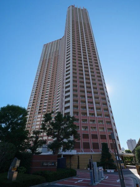 高層のビルと青空、手前に木と駐車場の風景