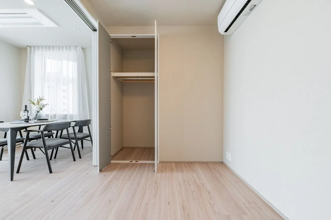 空のクローゼットとダイニングルームの一部、木製の床と白い壁、エアコンが設置されている部屋の写真