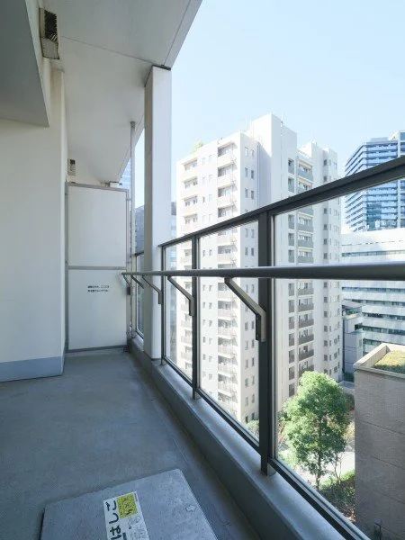 高層ビルの上層階のバルコニー。手すりとガラスの柵があり、都市の景色と山のような建物が見える。