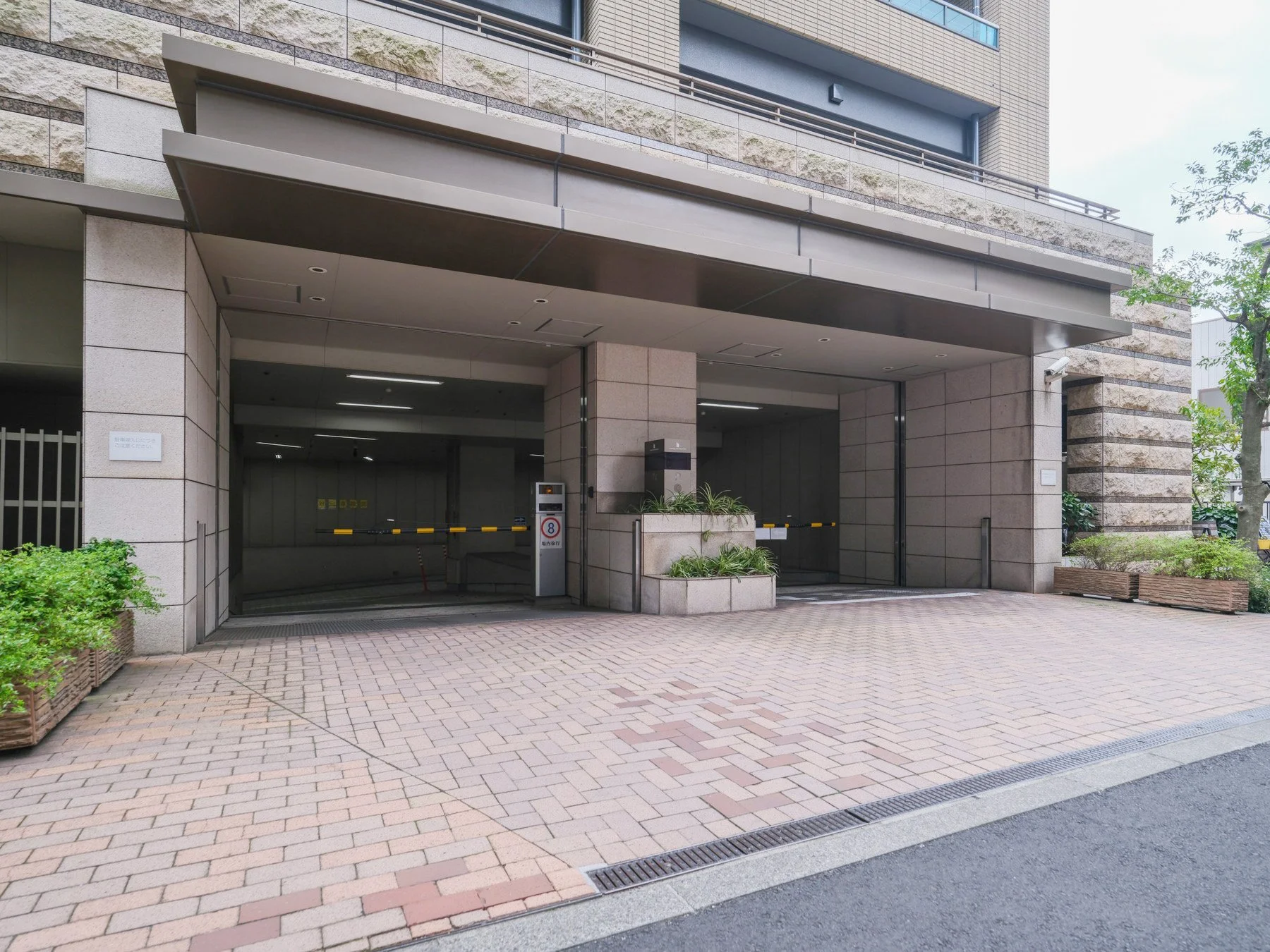 高層ビルの駐車場入り口。コンクリートの舗装路と小さな植栽が見える。