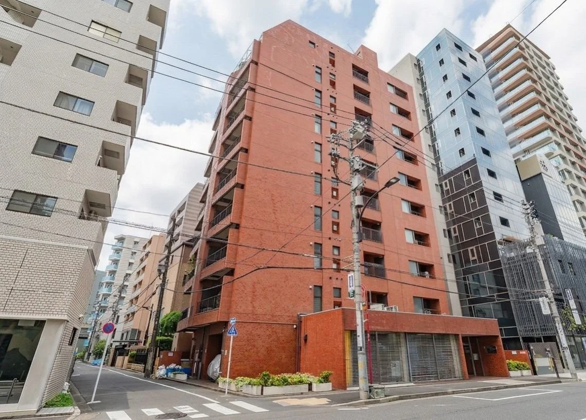 赤レンガの高層アパートメントビルと他の高層ビルが並んでいる都市の景色。電線や街路灯が映っている。
