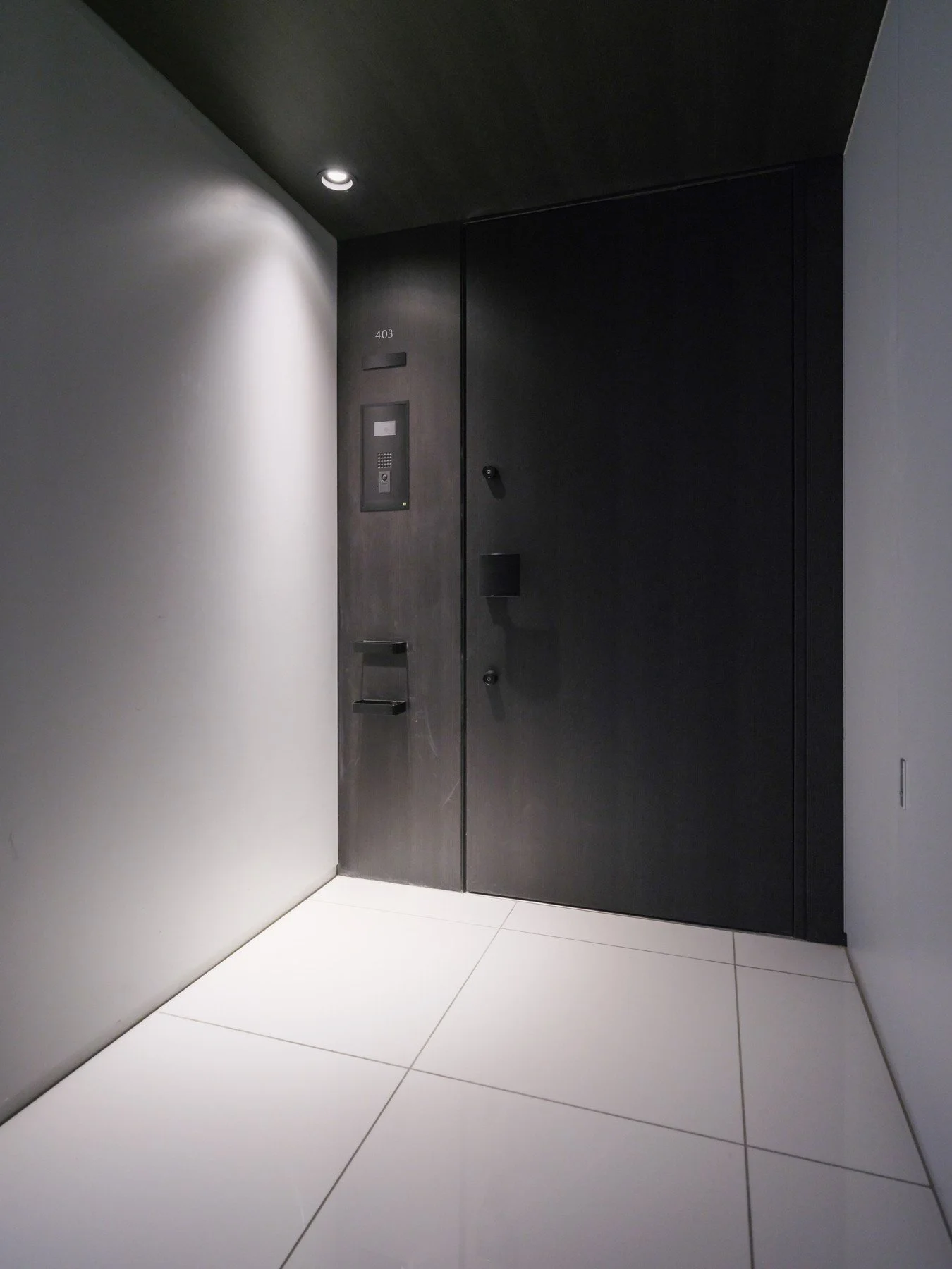 黒いドアとエレベーターの前の白いタイルの床、天井にはライトがあります。