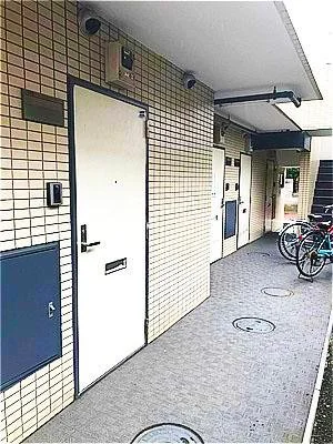 アパートやマンションの共用部分の廊下。扉やバイク、壁に設置された郵便受けや換気口が見える。