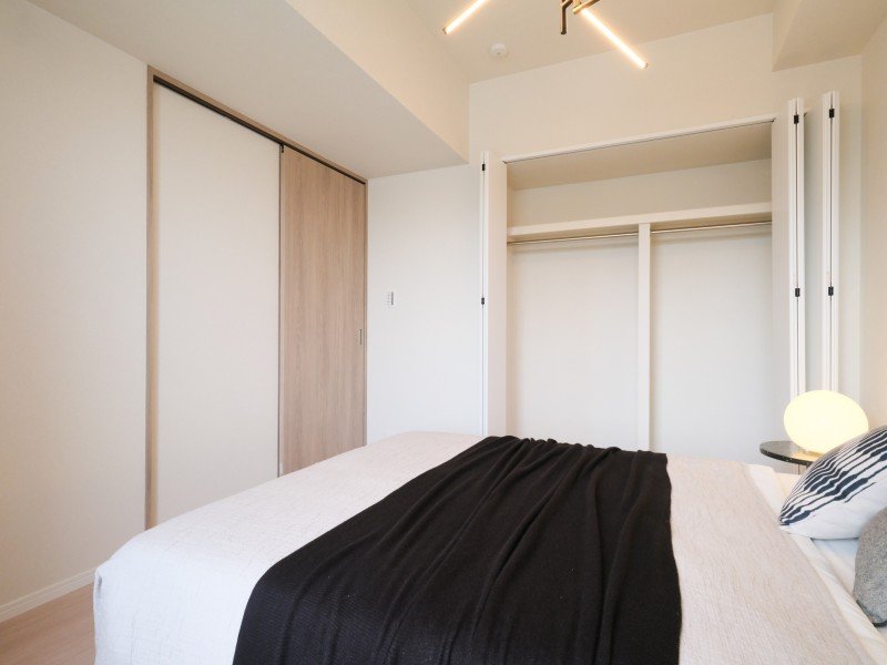 白い壁の部屋に、クローゼットとベッドがあり、ベッドには黒い布と枕が置かれている。