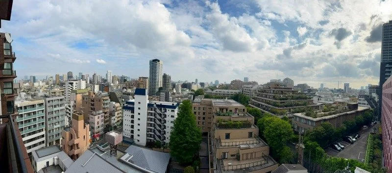 都市の高層ビルとマンションが立ち並ぶ景色。青い空と白い雲も見える。