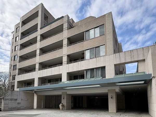 現代的な多層のコンクリート建築のマンション。入り口には屋根付きの歩道と装飾的な壺が配置されている。