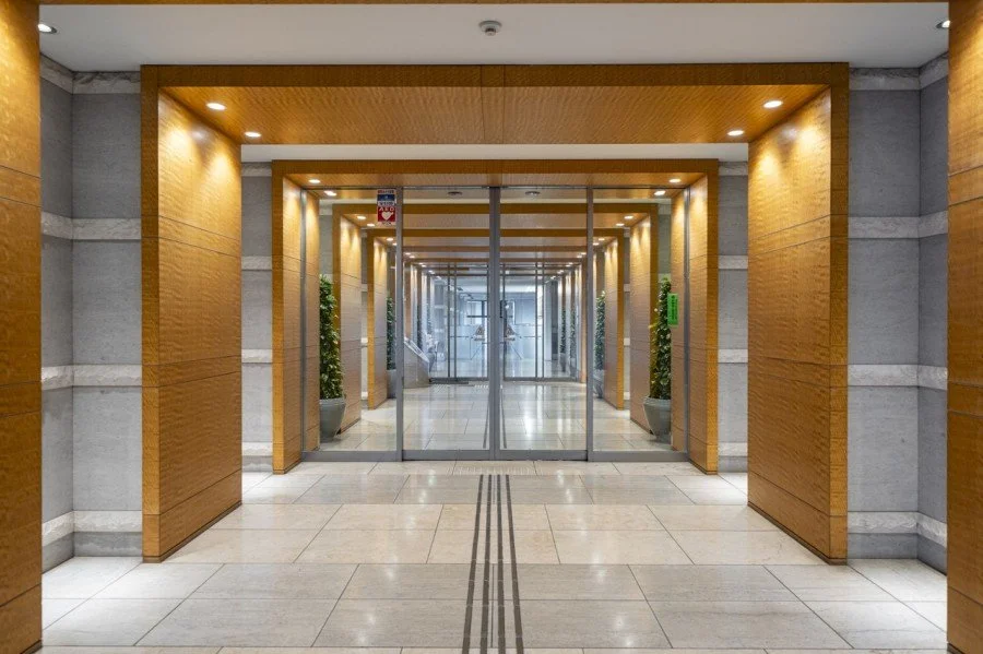 オフィスビルのエントランスの内部、ガラス扉と木製の枠、両側に観葉植物が置かれている