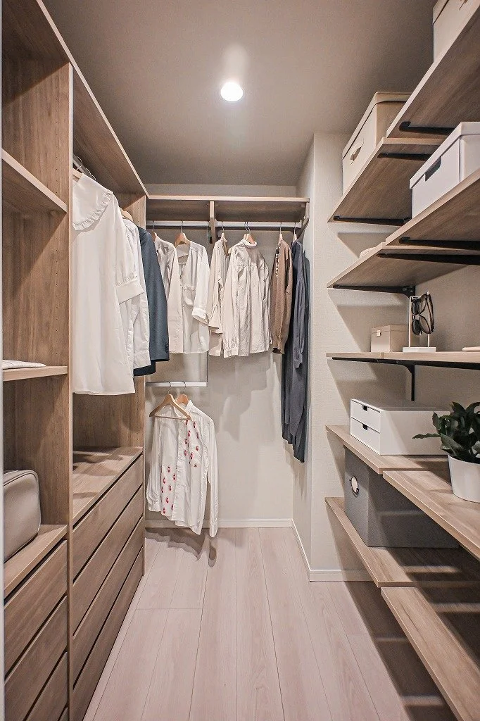 クローゼットの中に白と淡い色の衣服が掛かっている。棚や収納ボックスも見えるシンプルな収納空間