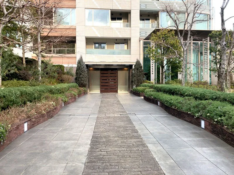 都市の高層マンションの入口付近、舗道と緑の植栽が整備されている