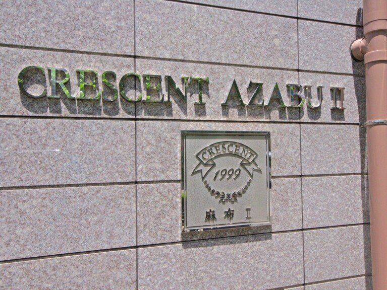 灰色のタイルの壁に緑色の立体文字で 『CRESCENT AZABU』と書いてある。看板の下に金属製のプレートがあり、『CRESCENT 1999 麻布工』と刻印されている。