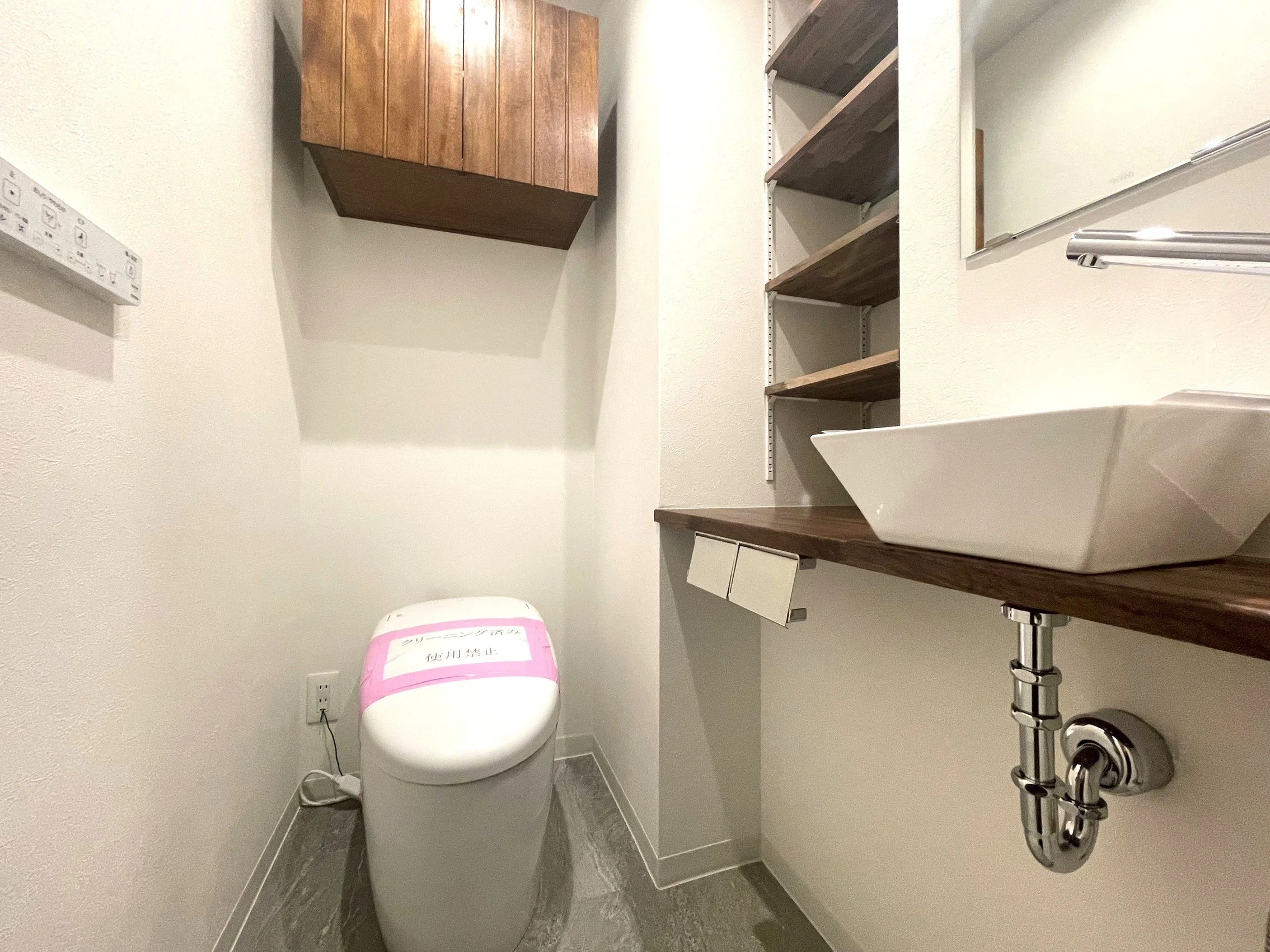 トイレの便器と棚、壁のスイッチと取っ手が見える。