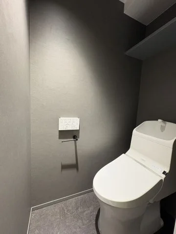 トイレが設置された小さな洋式便所。壁にリモコンとペーパーホルダーが付いている。