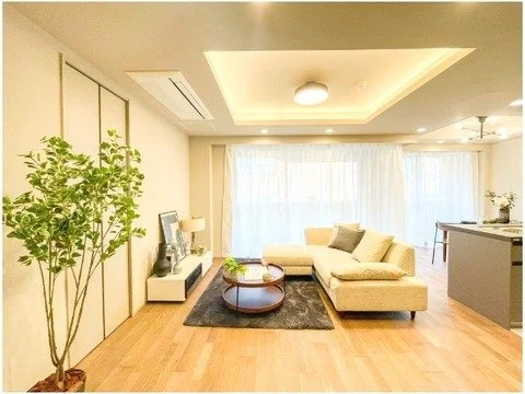 リビングルームに白いソファと円形のコーヒーテーブル、テレビと観葉植物が置かれている明るい室内