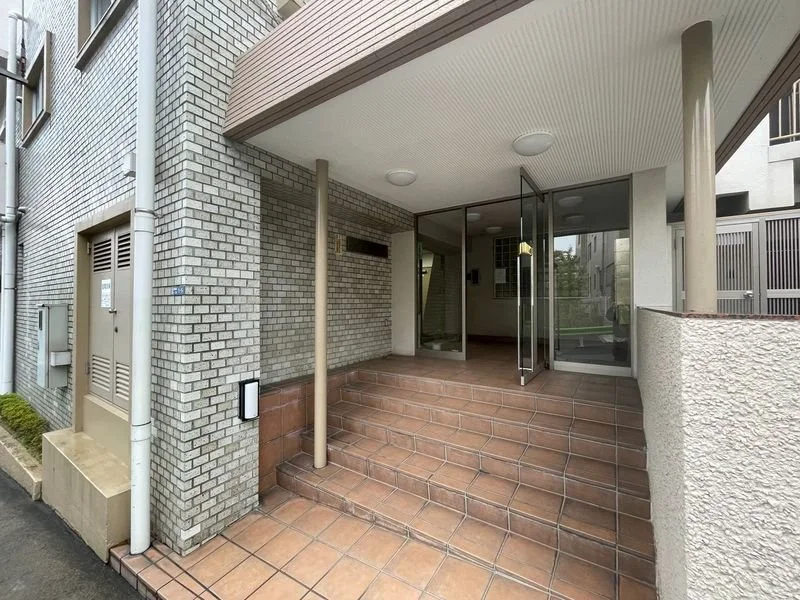 ビルのエントランスの階段とドア、ガラスの扉と窓、外壁はレンガとコンクリートで構成された建物の入り口部分。