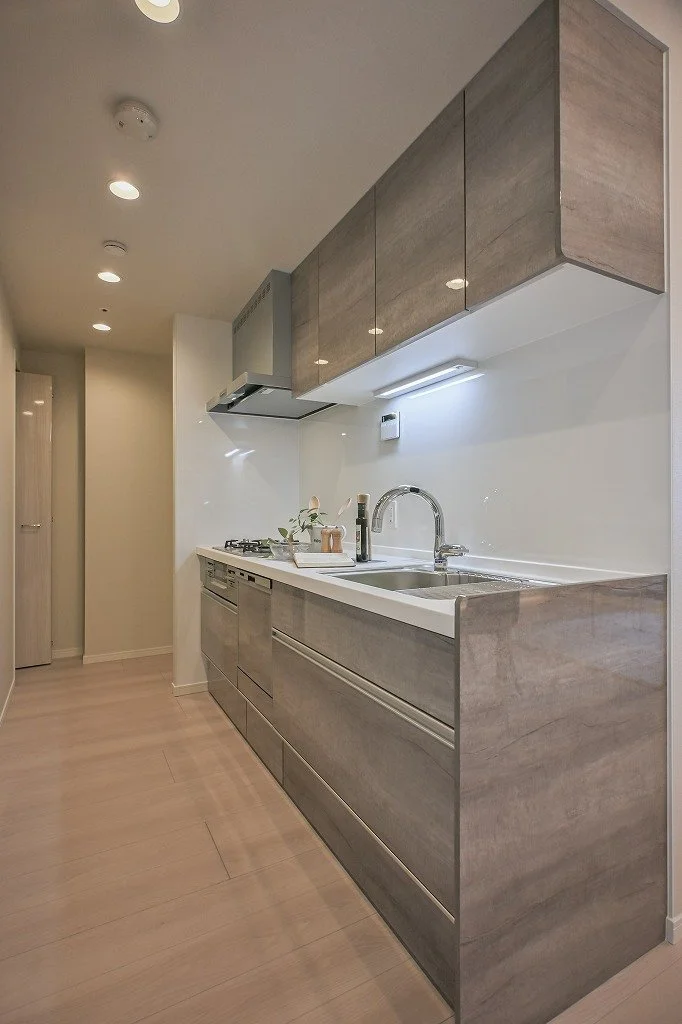 モダンなキッチンの内部、シンク、コンロ、木目調のキャビネット、白い壁とライトの照明