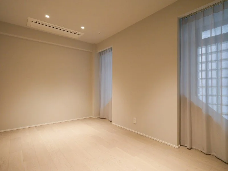 空の部屋で、白い壁と木製の床、窓にカーテンが引かれているシンプルなインテリア