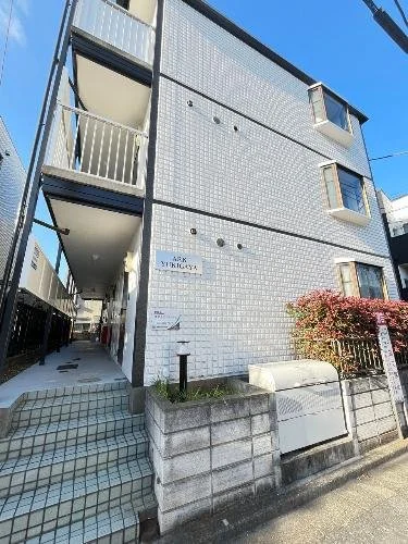 白いタイル張りの三階建ての建物と階段、バルコニーが見える