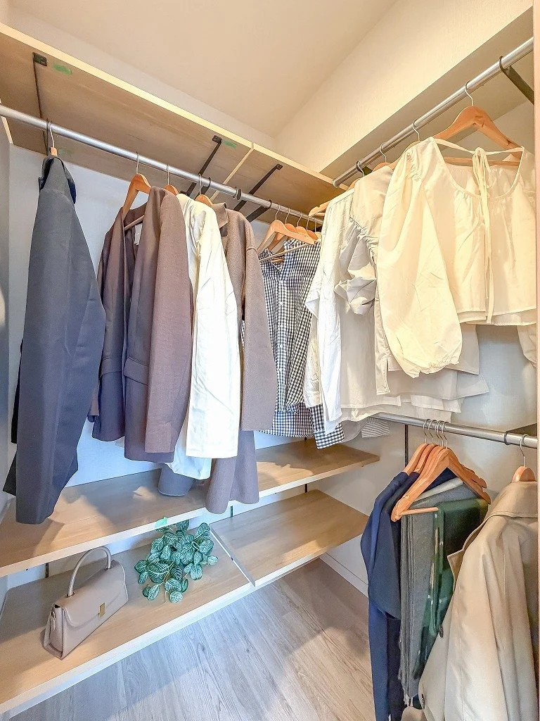 衣服が掛かっているクローゼットの中の収納棚とハンガーラック。スーツ、シャツ、ワンピースなどの衣服が整理されている。
