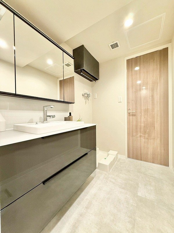 白い洗面台と大きな鏡、木目調の扉と暗いグレーの収納キャビネットがあるモダンな洗面所