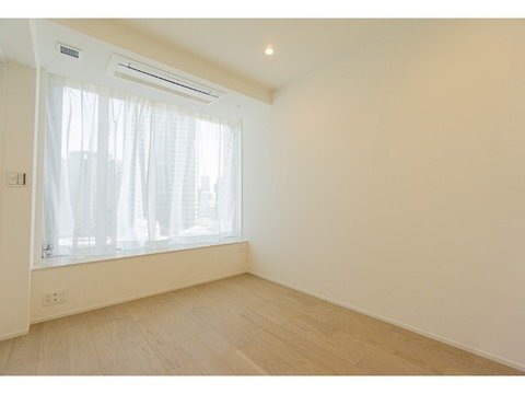 白い壁と木製の床を持つ、窓から自然光が入る空き部屋