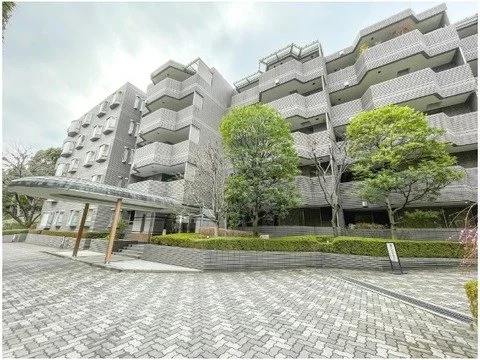 高層のマンション建物と前の広い歩道、木々が配置された都市風景