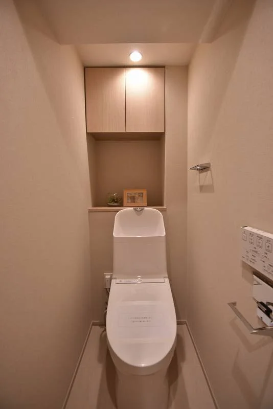 コンパクトなトイレルームにウォシュレット付きの便座と収納棚がある