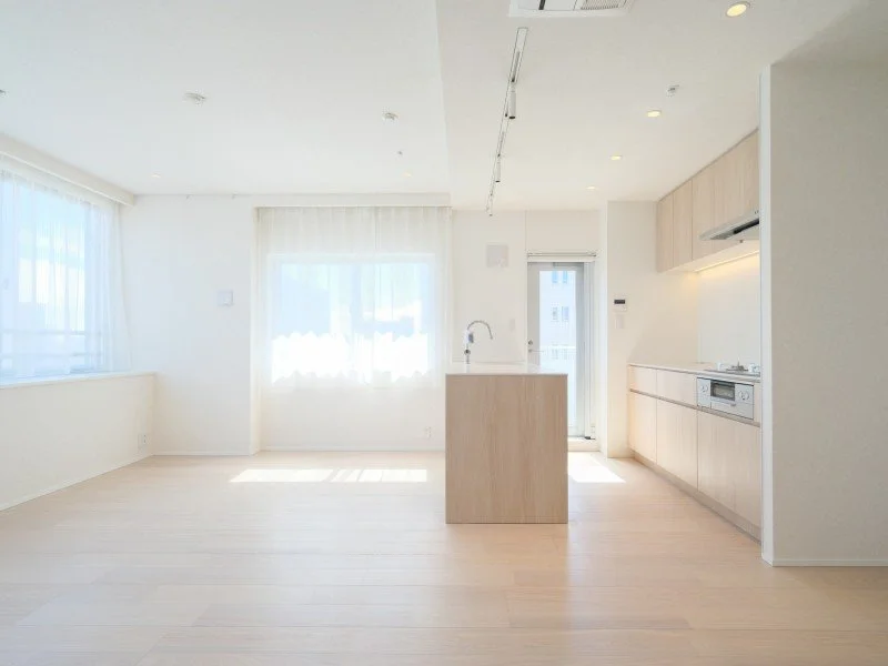 白を基調としたシンプルなキッチンとリビングルーム。大きな窓とガラスドアから自然光が差し込む明るい空間です。食洗器やコンロが備え付けられたキッチンカウンター付きのキッチンエリアがあります。