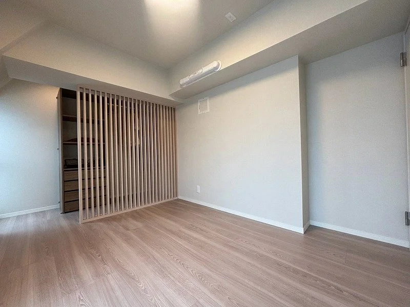 空の部屋で、木製の床と白い壁、木のスラットの仕切りがある。