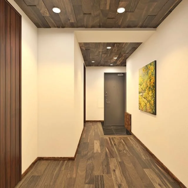 シンプルな玄関ホールで、白い壁と木製の床、天井には木材のパネルが張られている。左側に木の縞模様の壁パネル、右側には風景の絵画が掛かっている。奥には金属製の灰色のドアが見える。